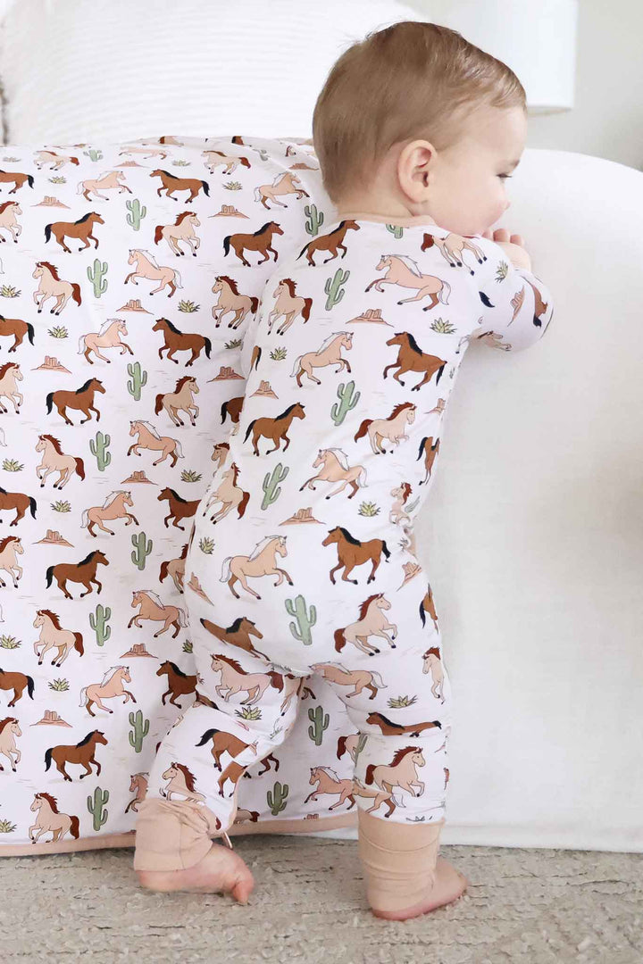baby boy walking along bed in pony club neutral convertible zip romper 