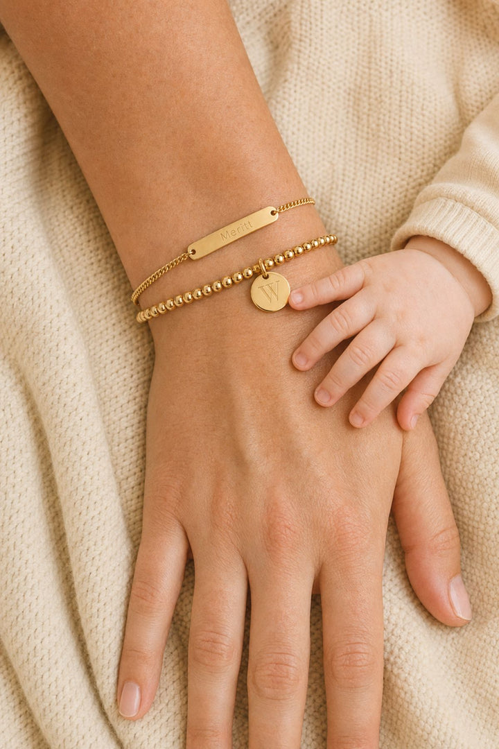 Caden Lane gold bracelet stack with engraved "Meritt" name bar and initial "W" disc charm, mother and baby holding hands