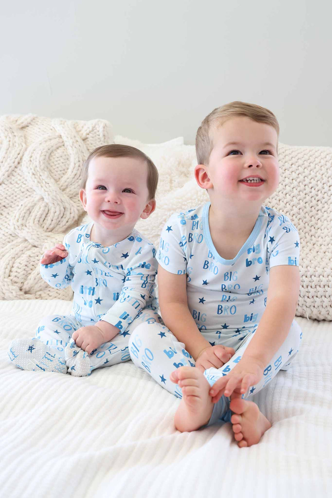 brothers sitting on bed wearing matching big bro and little bro pajamas 