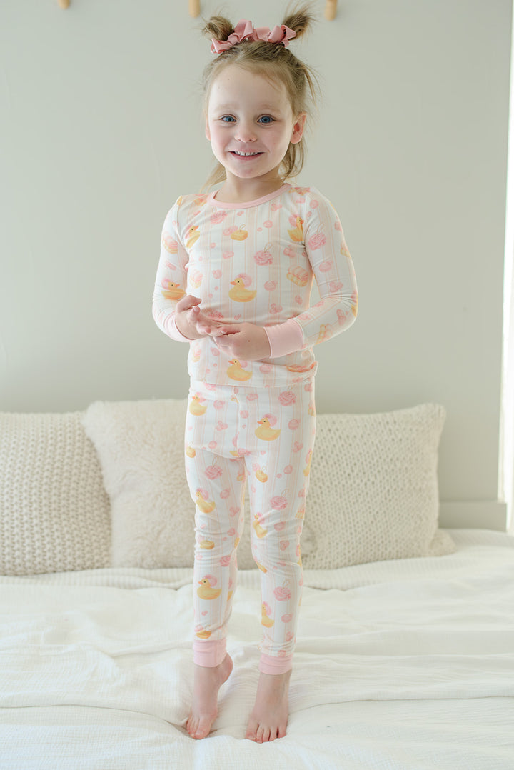Young girl standing on bed in pink Bubble Duckies two-piece bamboo pajamas with long sleeve top and full pants