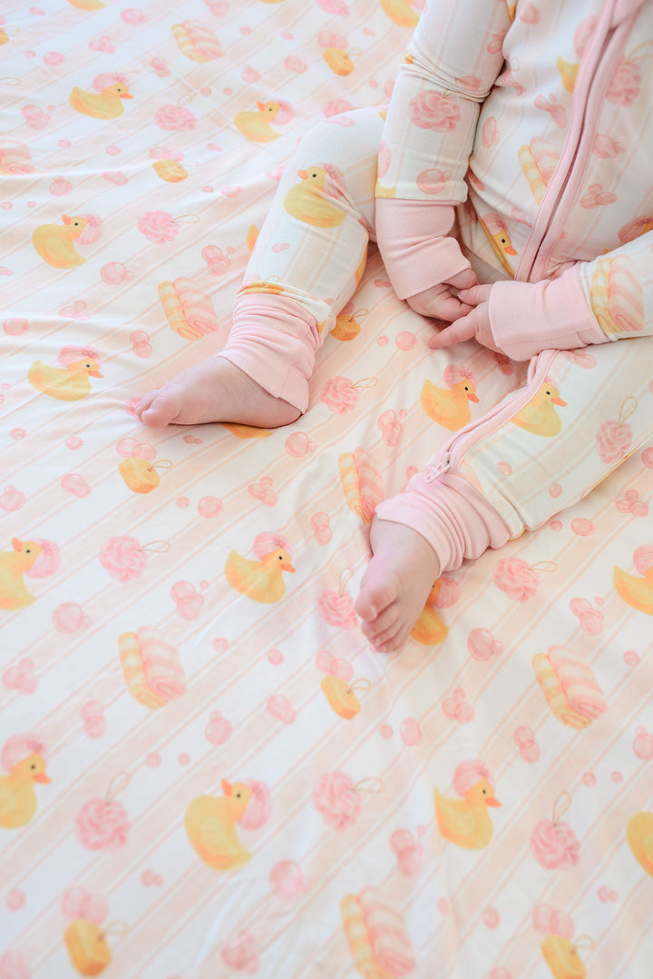 Child sitting on pink Bubble Duckies bamboo blanket wearing matching pink pajamas showing bare feet