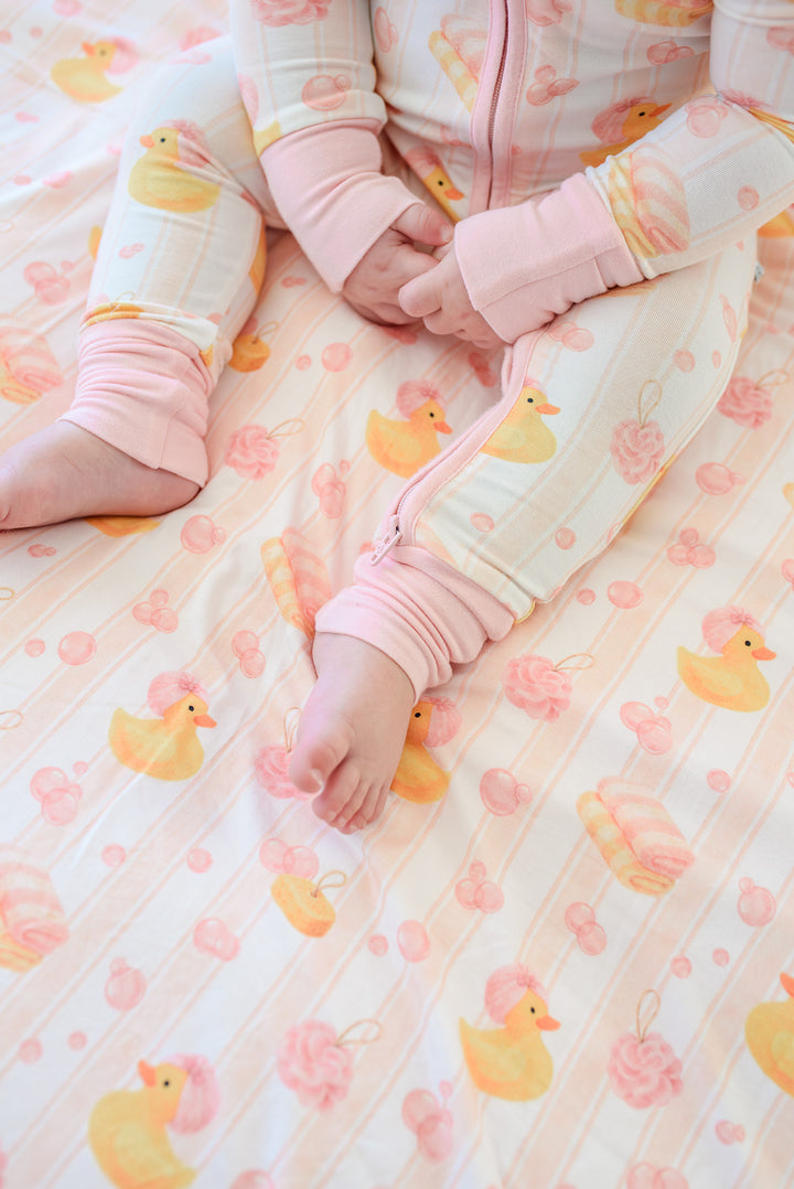 Close-up of child in pink Bubble Duckies pajamas sitting on matching bamboo blanket showing print detail