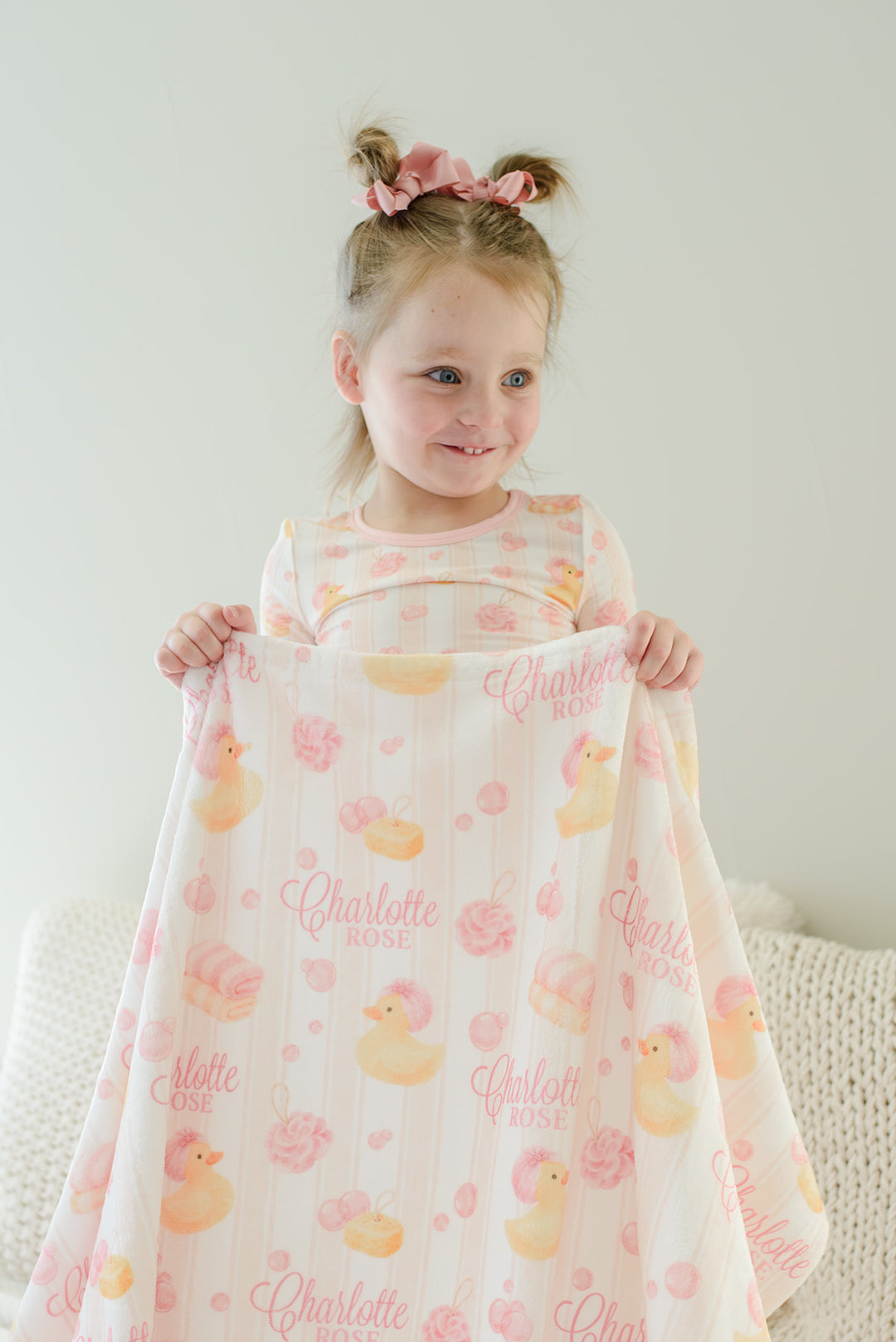 Young girl holding pink Bubble Duckies personalized kids blanket with yellow rubber duck and pink bubble print featuring custom name
