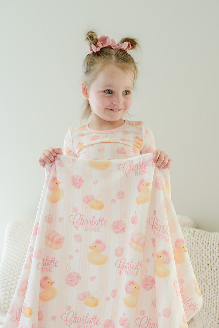 Young girl holding pink Bubble Duckies personalized kids blanket with yellow rubber duck and pink bubble print featuring custom name
