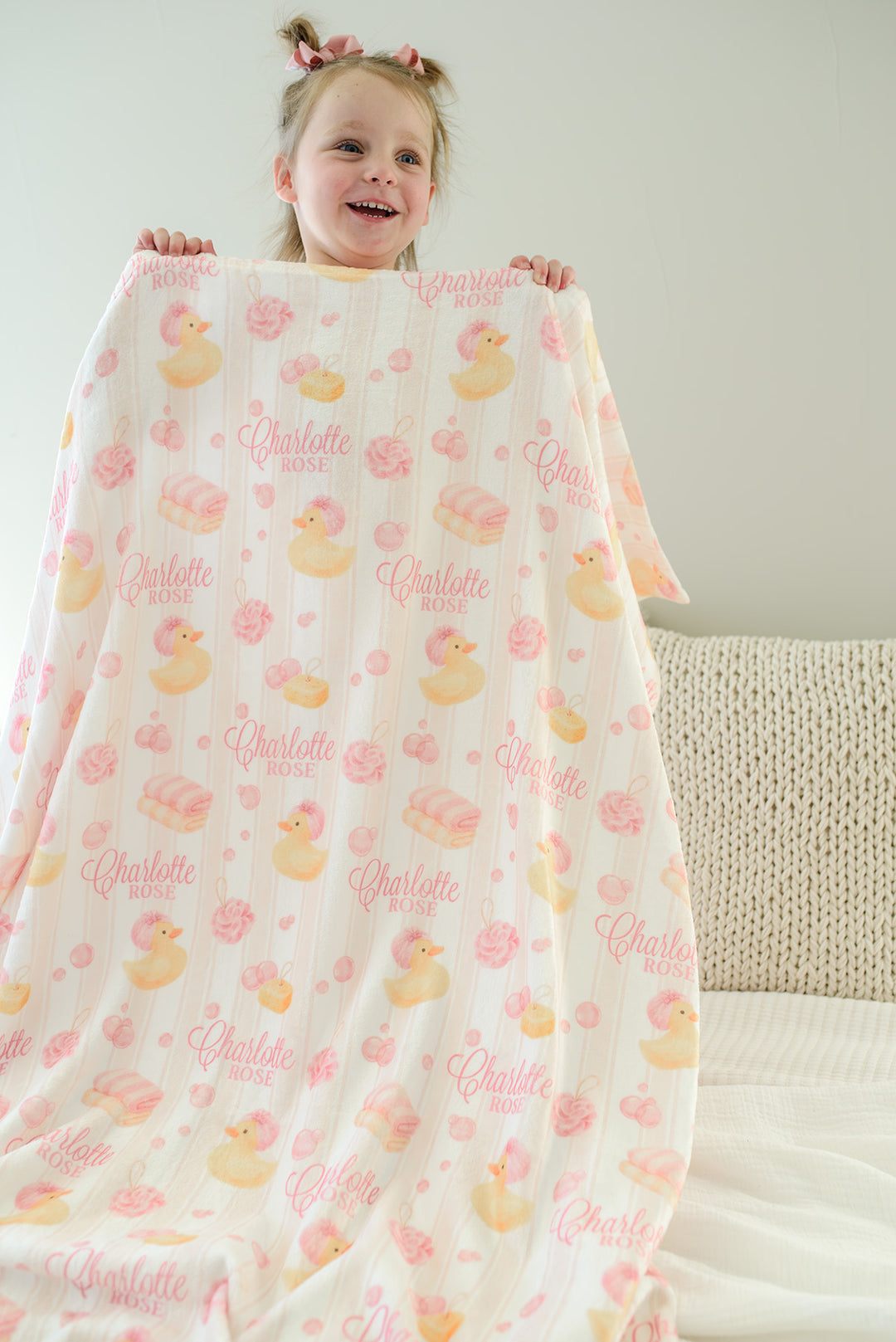 Young girl holding up pink Bubble Duckies personalized blanket with yellow rubber duck print and custom name