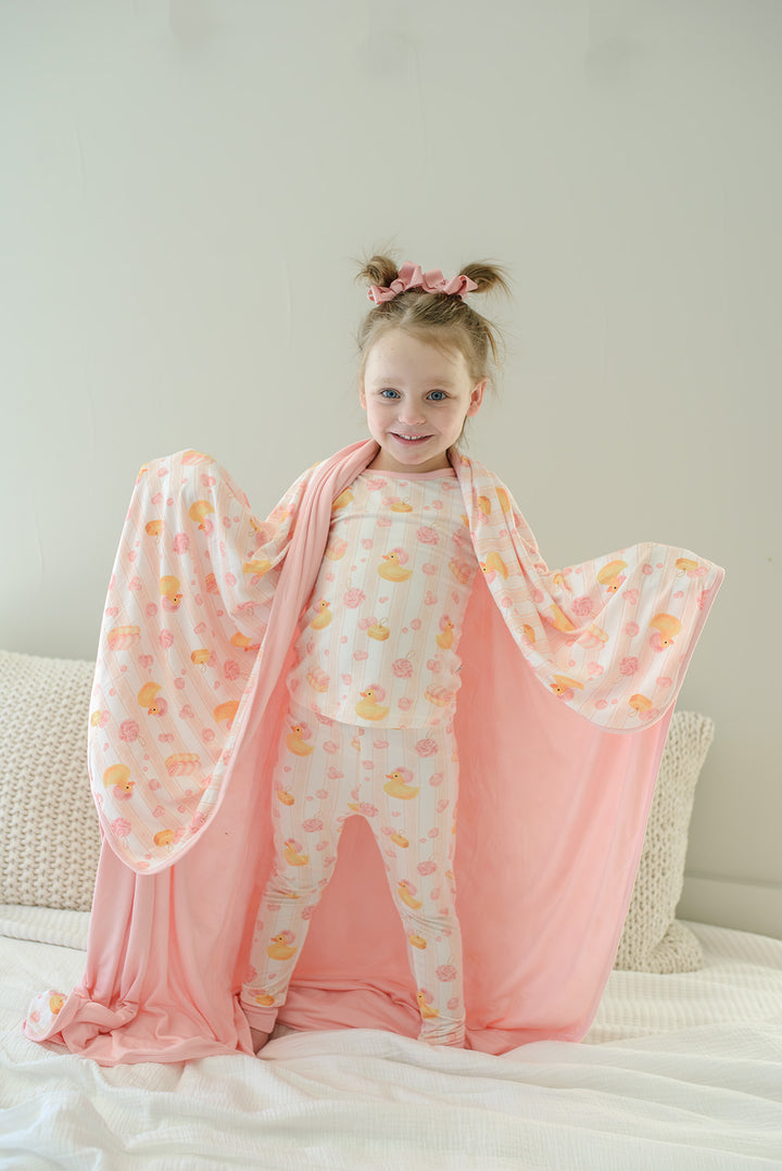 Young girl holding up pink Bubble Duckies double-sided bamboo blanket showing printed front and solid pink back