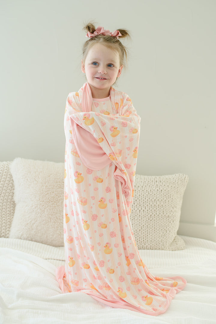 Young girl wrapped in pink Bubble Duckies double-sided bamboo blanket with yellow rubber duck print