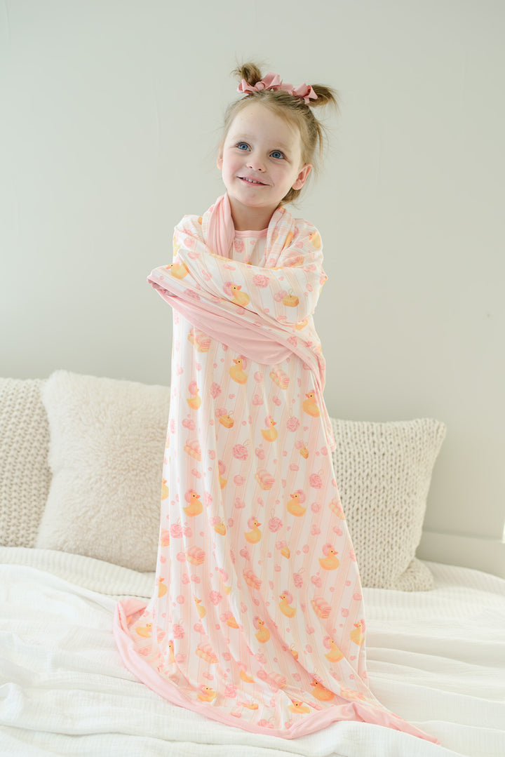 Young girl standing and wrapped in pink Bubble Duckies double-sided bamboo blanket with rubber duck print
