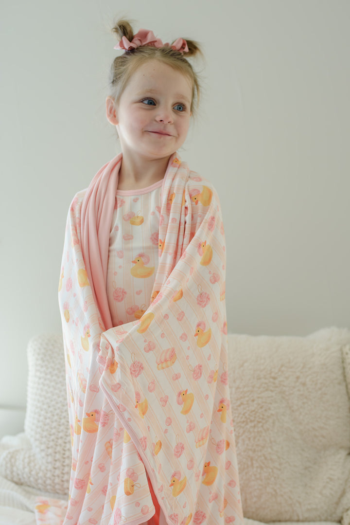 Young girl draped in pink Bubble Duckies bamboo blanket with yellow rubber duck and pink rose print