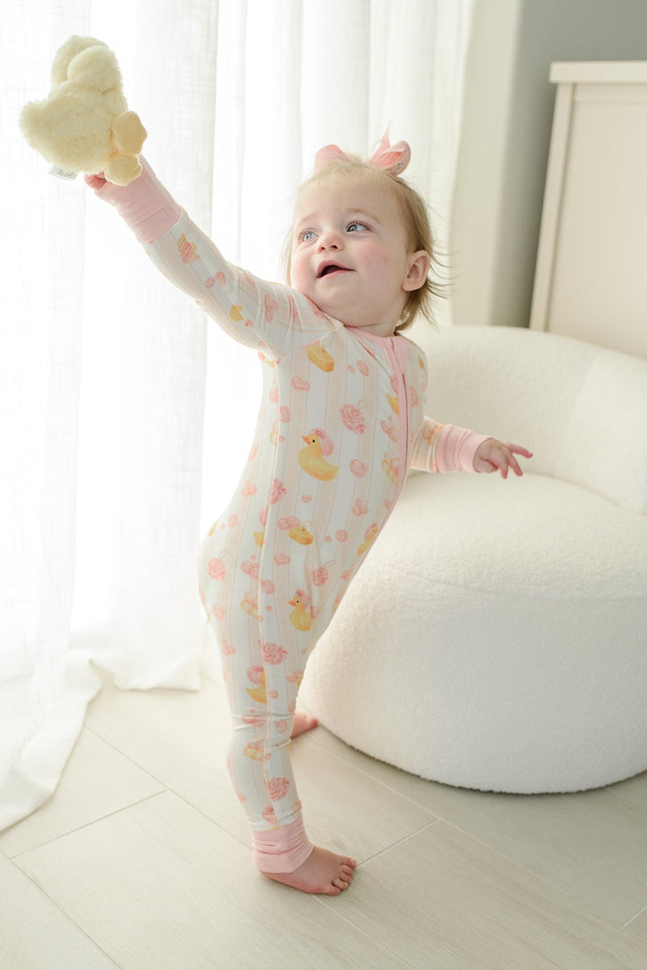 Baby girl with pink bow smiling in pink Bubble Duckies zip romper on matching duck print bedding