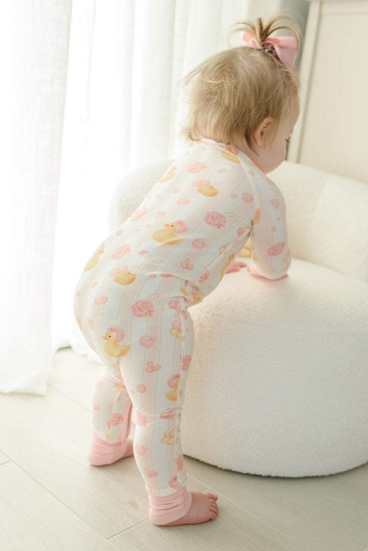 Baby girl laughing in pink Bubble Duckies convertible zip romper with matching duck print sheets and white pillow