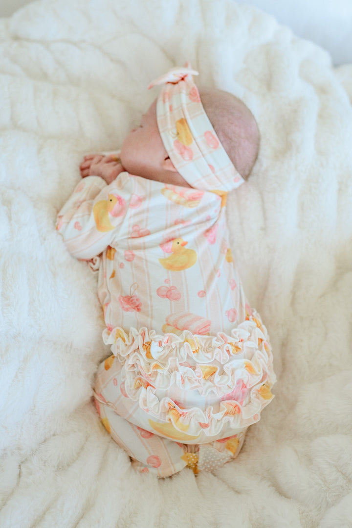 Overhead view of newborn in pink Bubble Duckies ruffle footie pajamas on white fur showing ruffle bottom