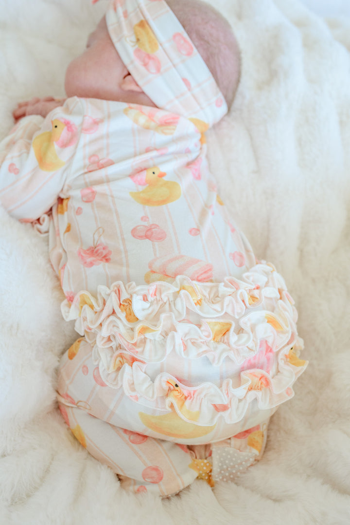 Top view of sleeping newborn in pink Bubble Duckies ruffle zipper footie on white fur showing ruffle bottom detail