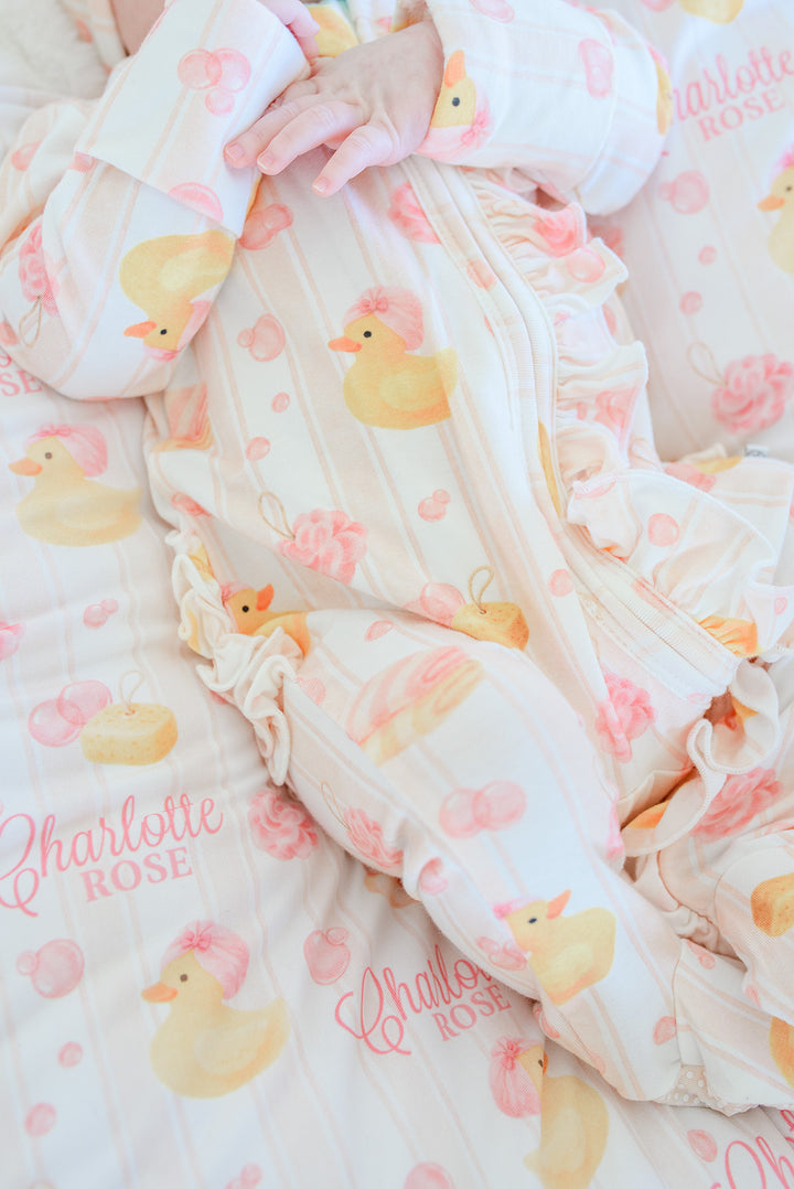 Close-up detail of pink Bubble Duckies ruffle zipper footie on baby showing rubber duck print and ruffle hem