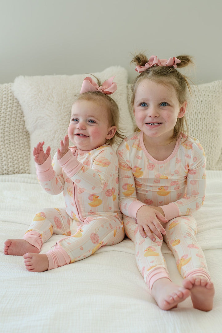 Cheerful baby girl in pink Bubble Duckies convertible zip romper sitting up on matching duck print bedding