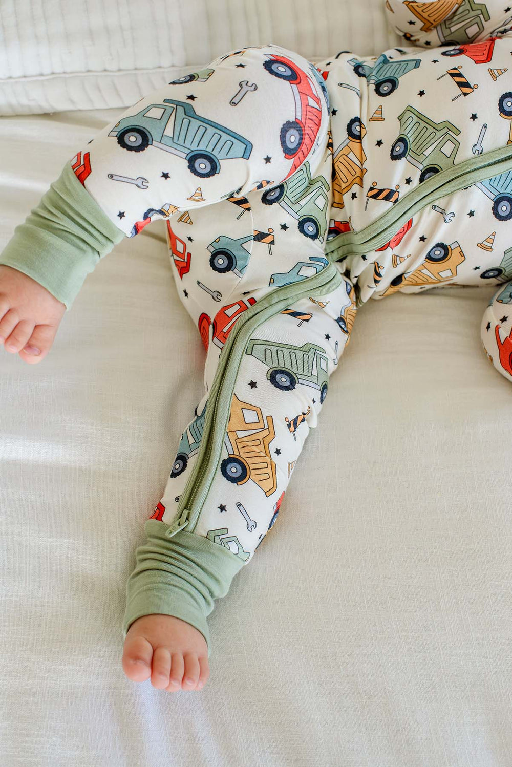 Close-up of a baby's leg showing the sage zipper running down a Caden Lane cream knit romper in a Busy Builder print featuring dump trucks.