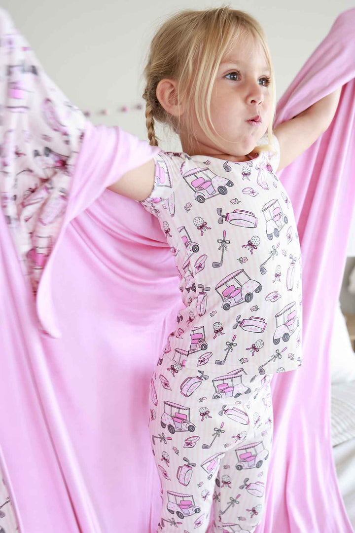 girl in pink caddie crew two piece pajama set with matching blanket wrapped around her