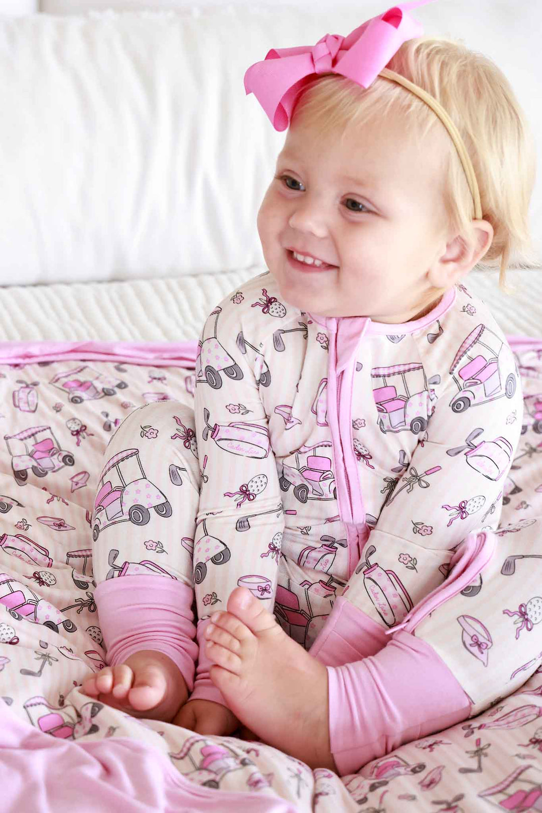 girl sitting on bed in pink convertible zip romper with a matching bamboo blanket