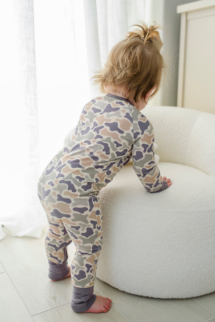 Baby toddler in camo cutie zip romper sitting on rug, back view