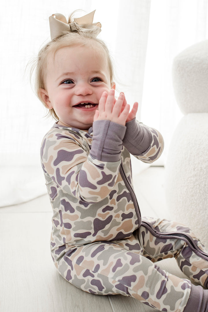 Baby toddler seen from behind in camo cutie convertible zip romper on a rug