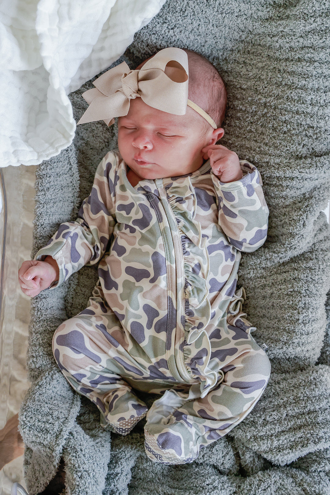 Close-up of newborn baby girl in a camo cutie print ruffle zipper footie wearing a taupe ribbon bow headband