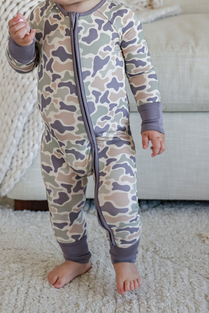 Baby toddler seated on a rug from behind wearing camo cutie zip romper