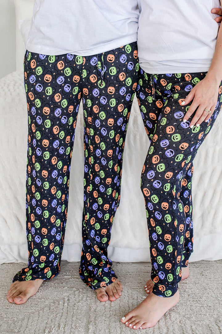 Close-up of two people standing in matching black bamboo waffle pajama pants with colorful jack-o-lantern candy print
