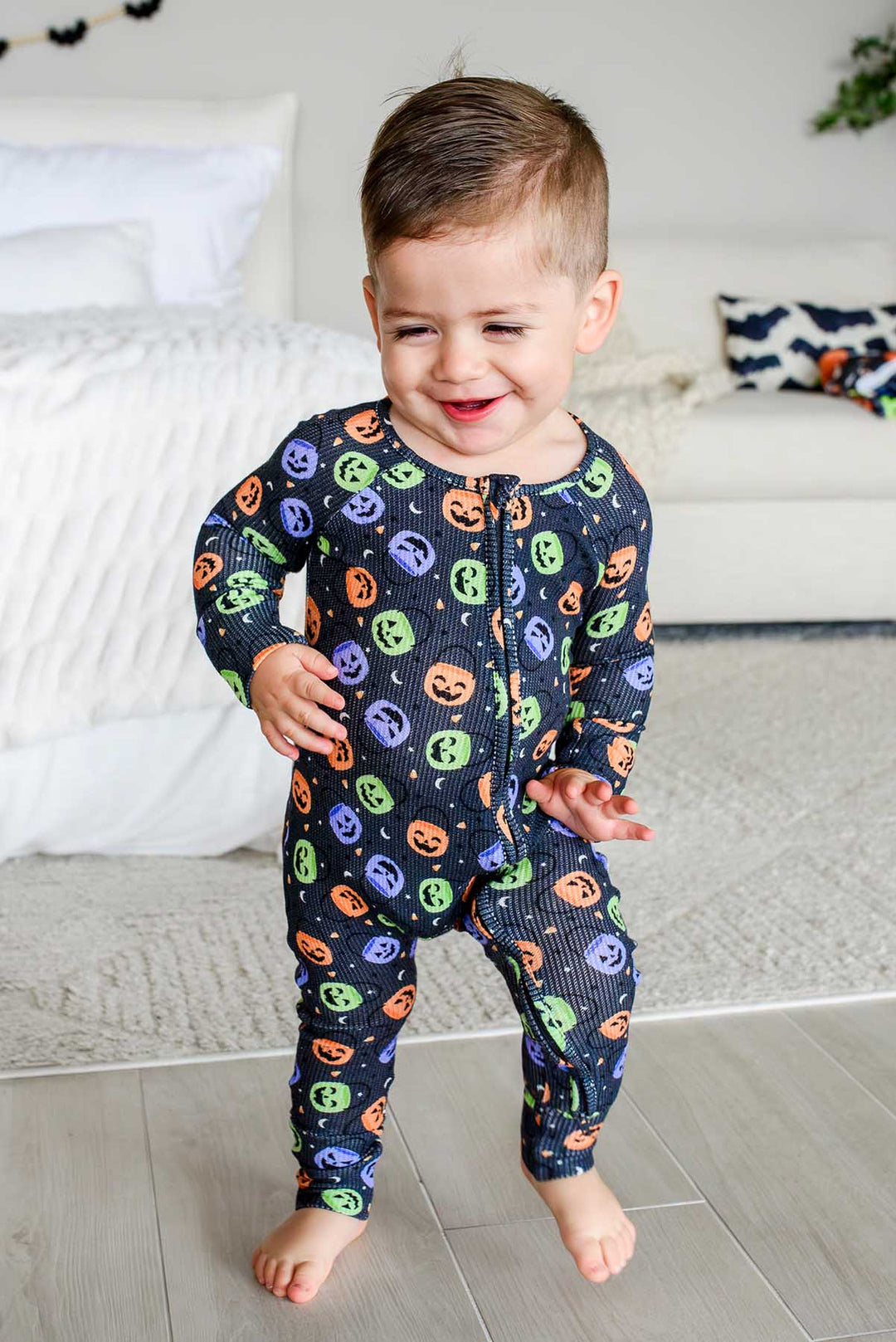 Toddler walking in a bamboo waffle romper with colorful jack-o-lantern print, smiling