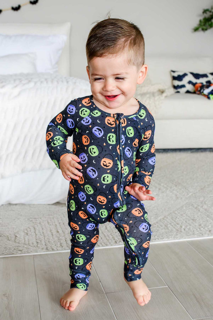 Toddler walking in a bamboo waffle romper with colorful jack-o-lantern print, smiling