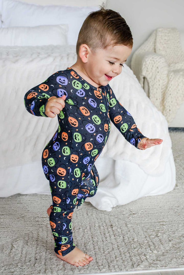 Toddler playfully dancing on a rug in a bamboo waffle romper with colorful jack-o-lantern print