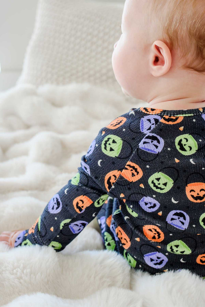 Close-up of a baby sitting on a fluffy blanket in a bamboo waffle romper with colorful jack-o-lantern print