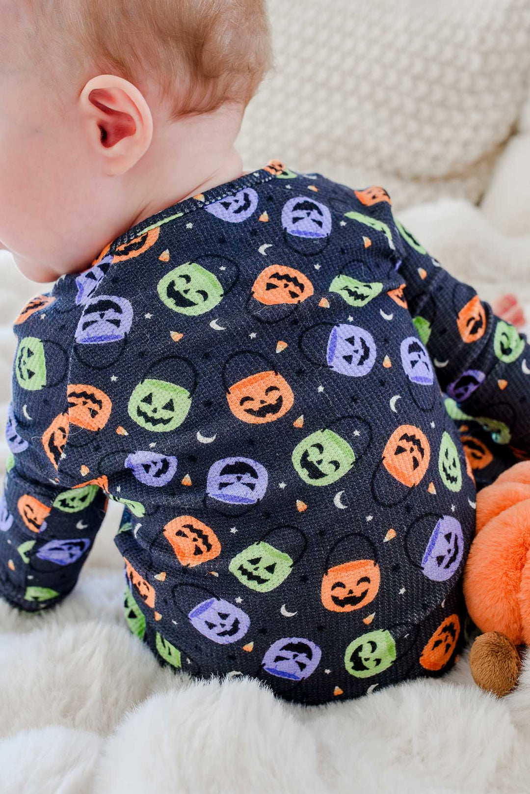 Close-up of a baby's back in a bamboo waffle romper with colorful jack-o-lantern print