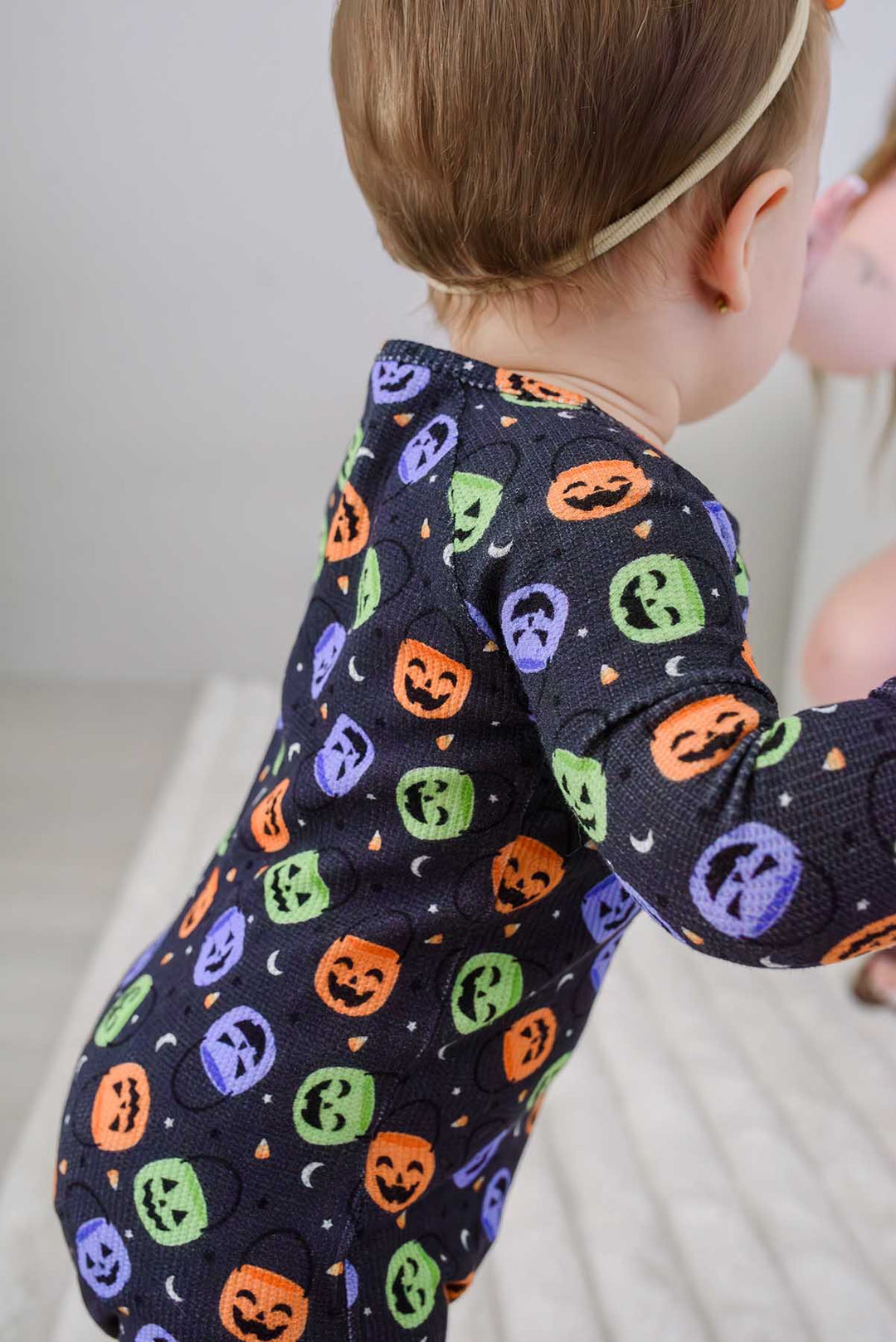 Close-up side view of a baby in a bamboo waffle romper with colorful jack-o-lantern print