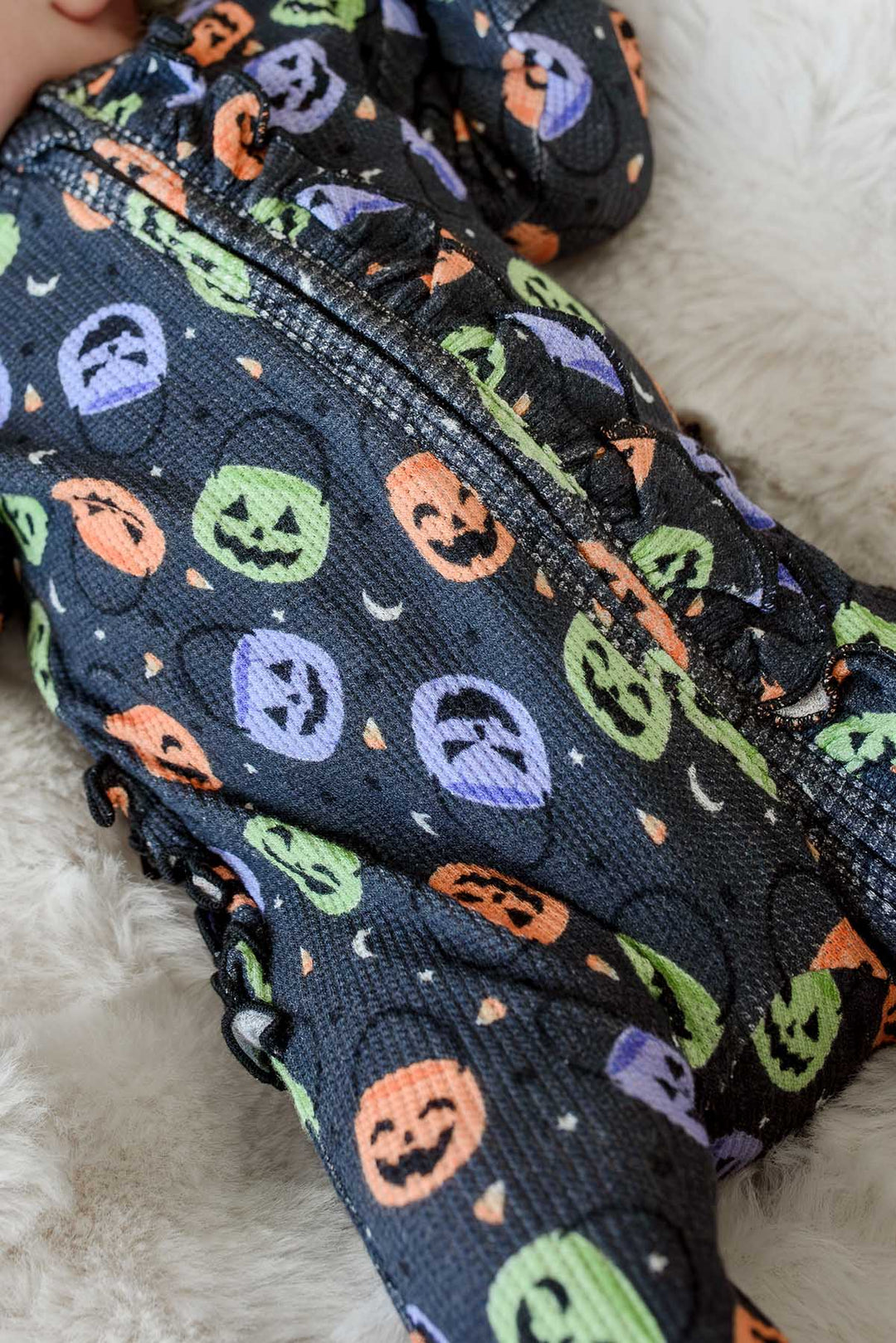 Close-up of a bamboo waffle ruffle zipper footie with colorful jack-o-lantern print on a sleeping baby