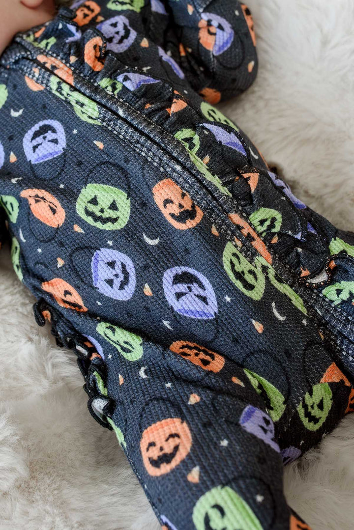 Close-up of a bamboo waffle ruffle zipper footie with colorful jack-o-lantern print on a sleeping baby