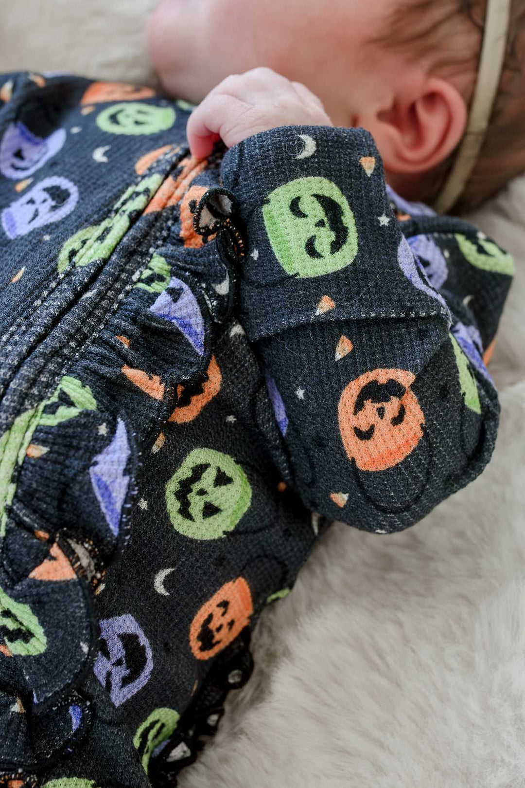 Close-up of a sleeping newborn's feet in a bamboo waffle ruffle footie with colorful jack-o-lantern print