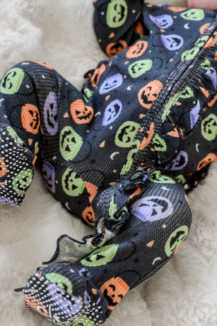 Close-up of a baby's legs and feet in a bamboo waffle ruffle footie with colorful jack-o-lantern print and polka dot footed bottoms