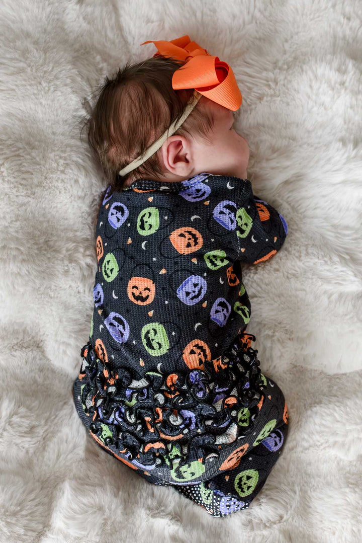 Back view of a sleeping baby with an orange bow wearing a bamboo waffle ruffle footie with colorful jack-o-lantern print, showing ruffle detail