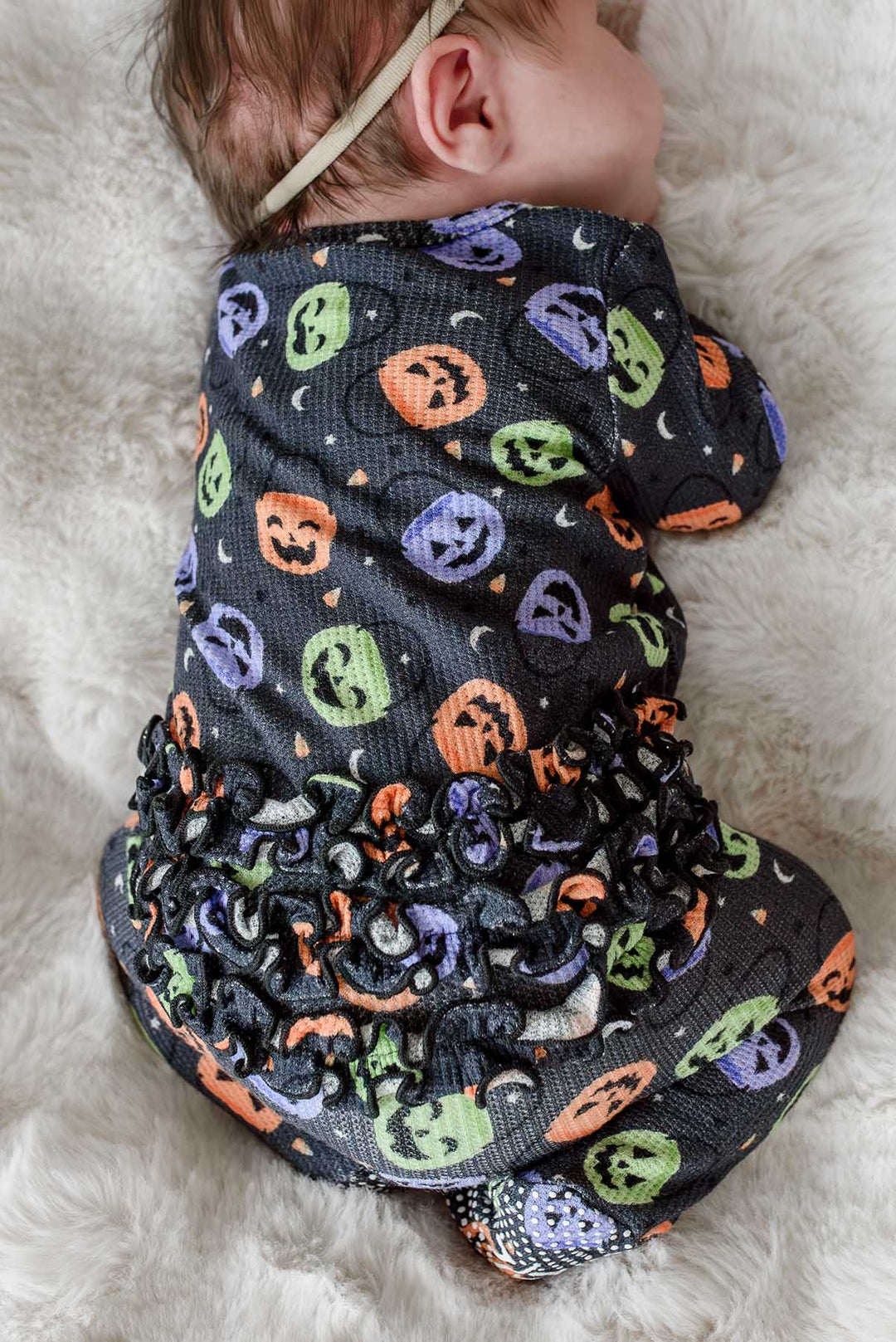 Close-up of a newborn wearing a bamboo waffle ruffle footie with colorful jack-o-lantern print, showing ruffle detail along the back and bottom