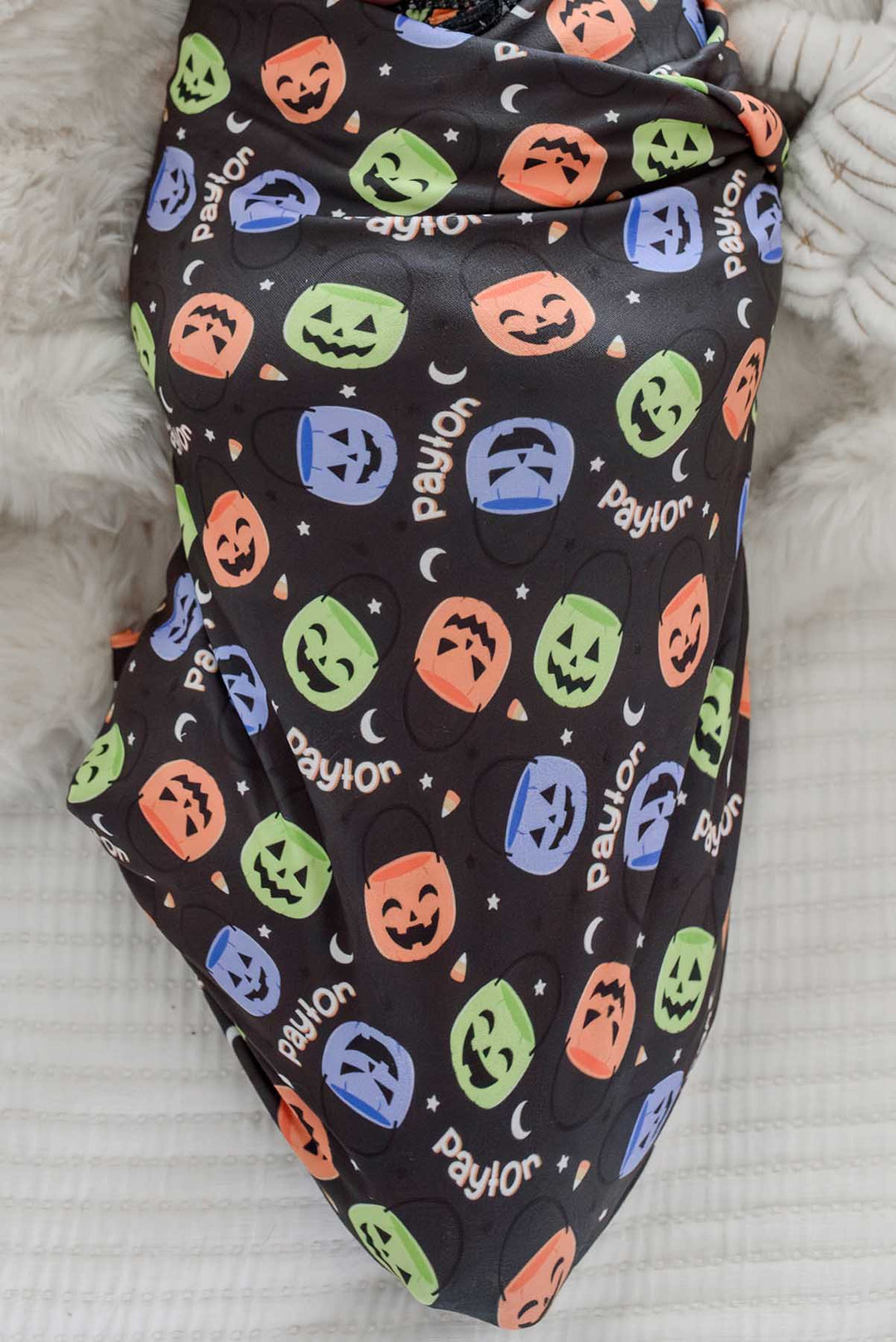 Close-up of a newborn swaddled in a personalized Halloween blanket with colorful jack-o-lantern print and repeating name text