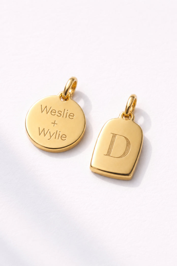 Caden Lane gold charms including engraved "Weslie + Wylie" disc pendant and initial "D" tag charm on white background