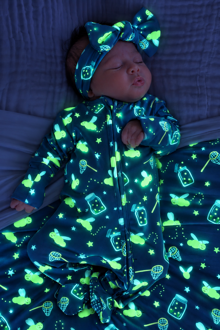 Overhead shot of a sleeping newborn on a matching blanket, wearing a Caden Lane blue bamboo zipper footie in a Chasing Fireflies print featuring fireflies and mason jars.