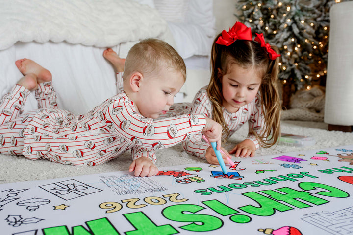 Toddler coloring a gift with a blue marker on a personalized Christmas coloring banner as his sister colors beside him