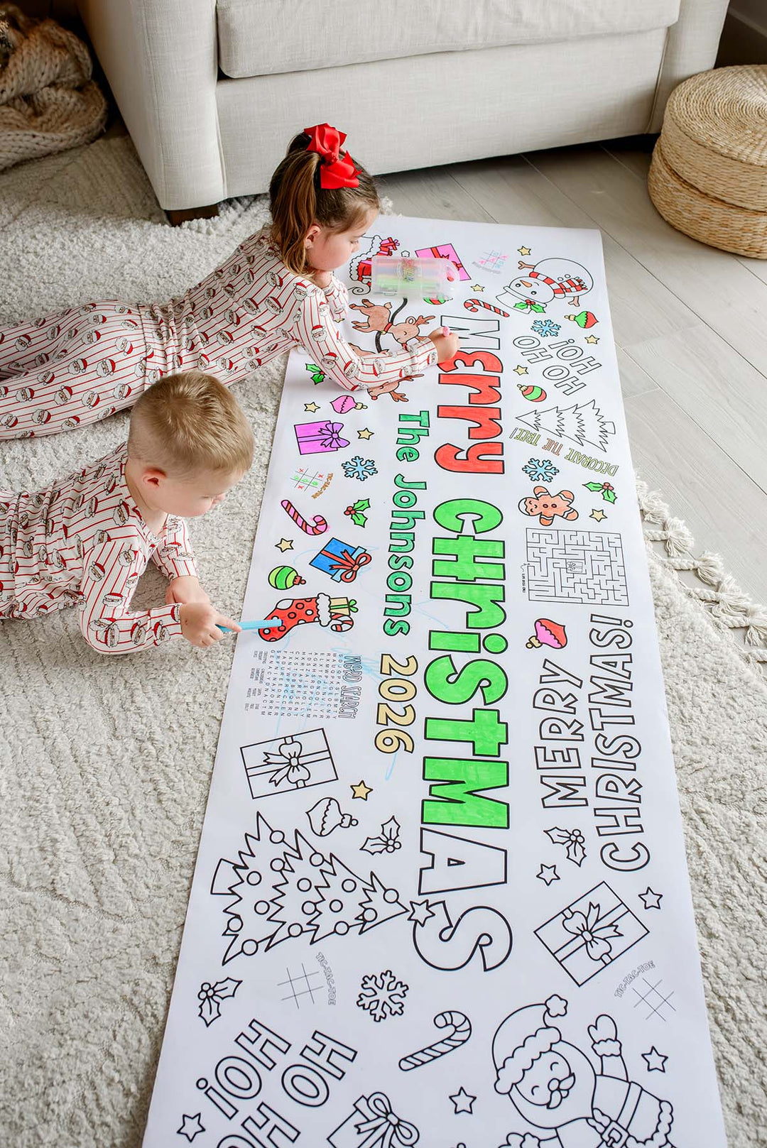 Overhead view of two kids coloring a Merry Christmas The Johnsons 2026 personalized coloring banner on a living room rug