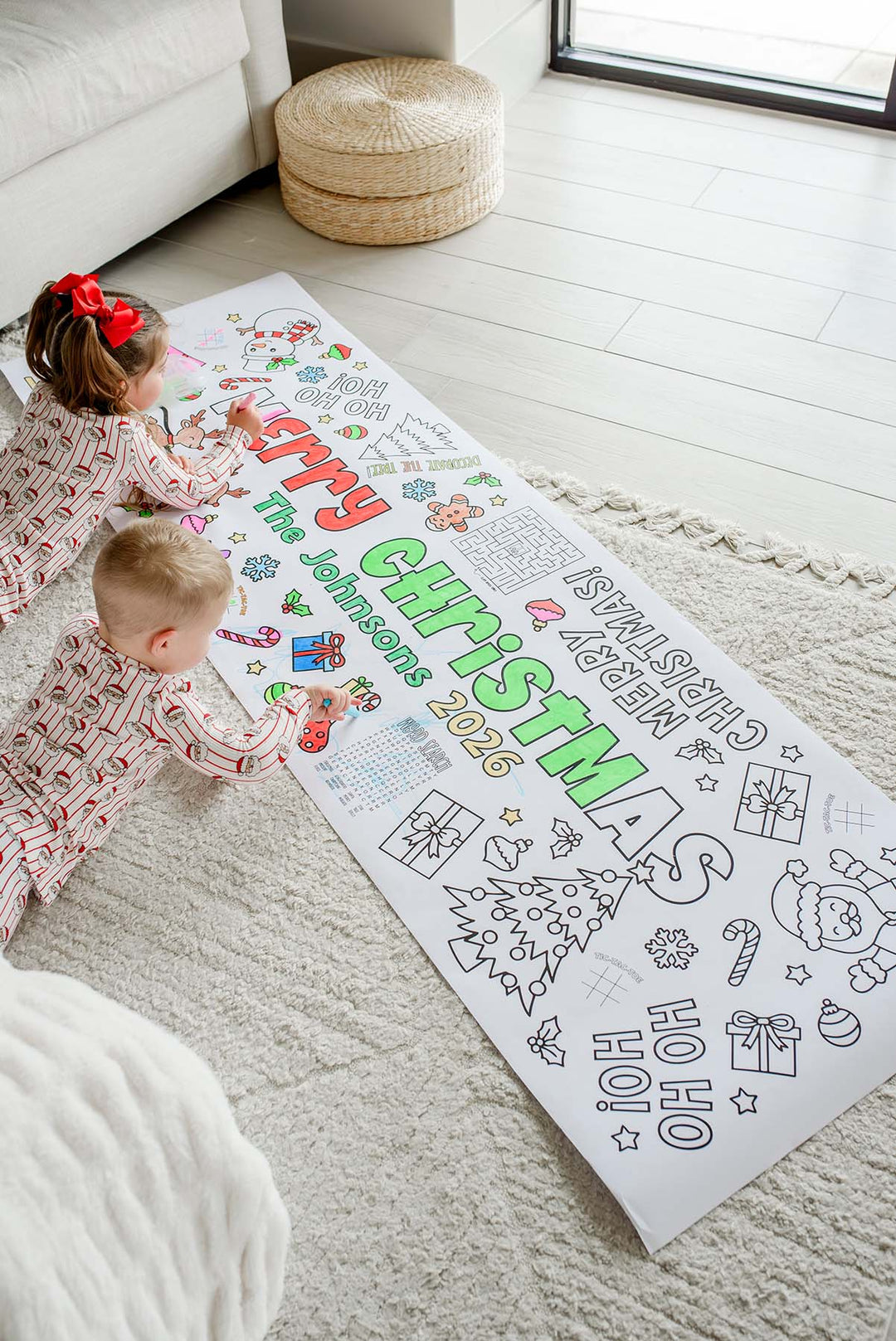 Siblings in matching Christmas pajamas coloring a long personalized Merry Christmas activity banner with a maze and word search
