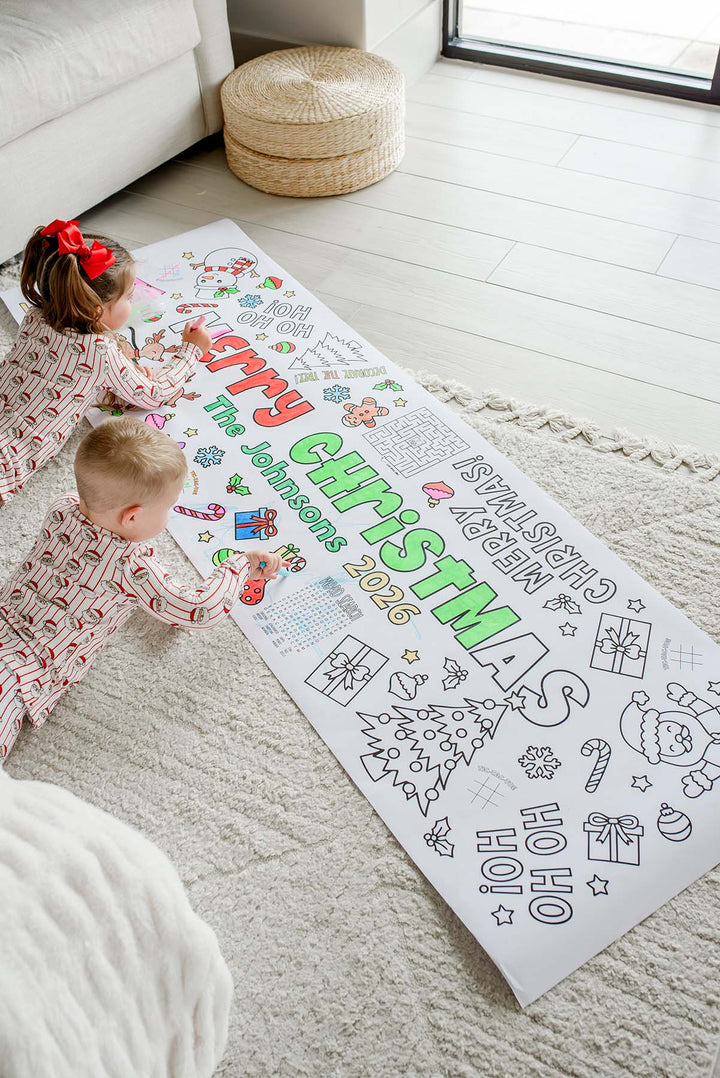 Siblings in matching Christmas pajamas coloring a long personalized Merry Christmas activity banner with a maze and word search
