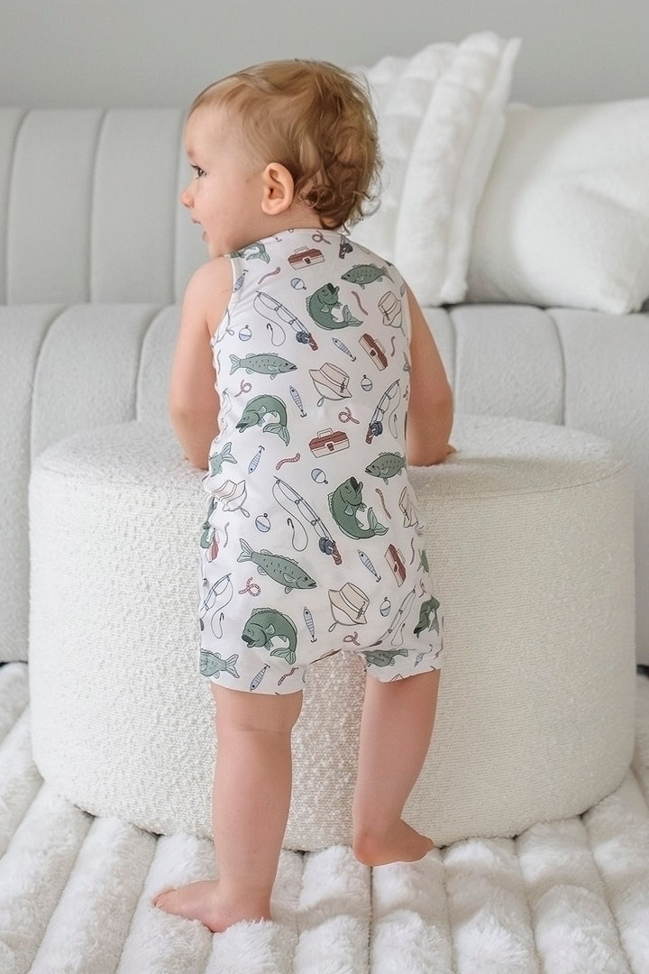 Baby standing facing away showing the back of the Off The Hook sleeveless snap romper with fishing print