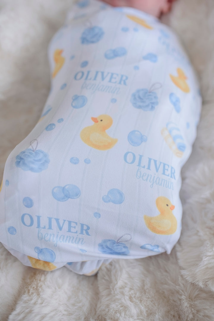 Close-up of baby swaddled in blue Bubble Duckies personalized blanket showing yellow rubber duck print and custom name