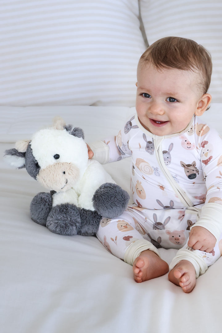 boy in farm pajama romper with arm around stuffed cow 