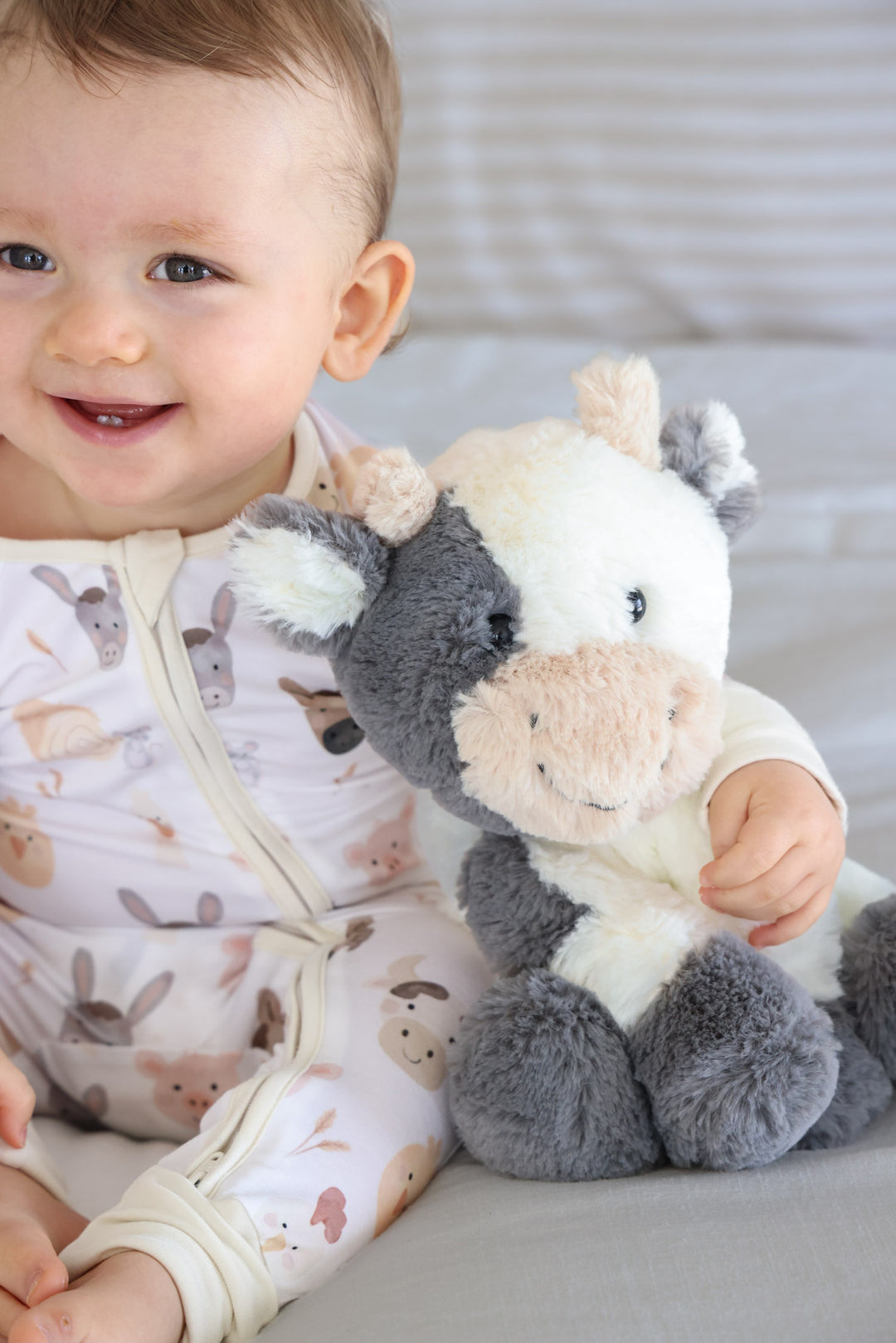 baby boy in farm pajamas with arm around cow stuffed animal